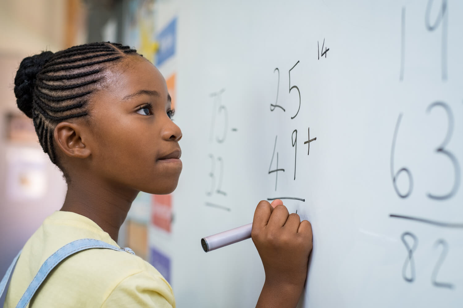 Close-up of a focused young student writing complex math equations on a whiteboard in a classroom.